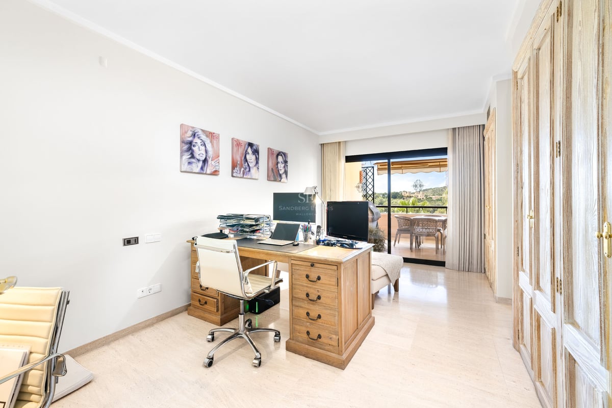 Bureau lumineux avec grand bureau en bois, chaise blanche et baies vitrées ouvrant sur une terrasse.