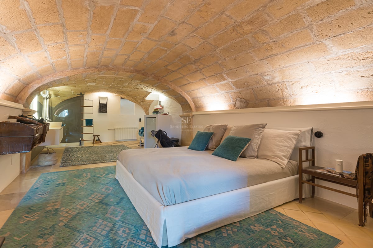 Chambre avec plafond voûté en grès, murs blancs, tapis turquoise et lit moderne.