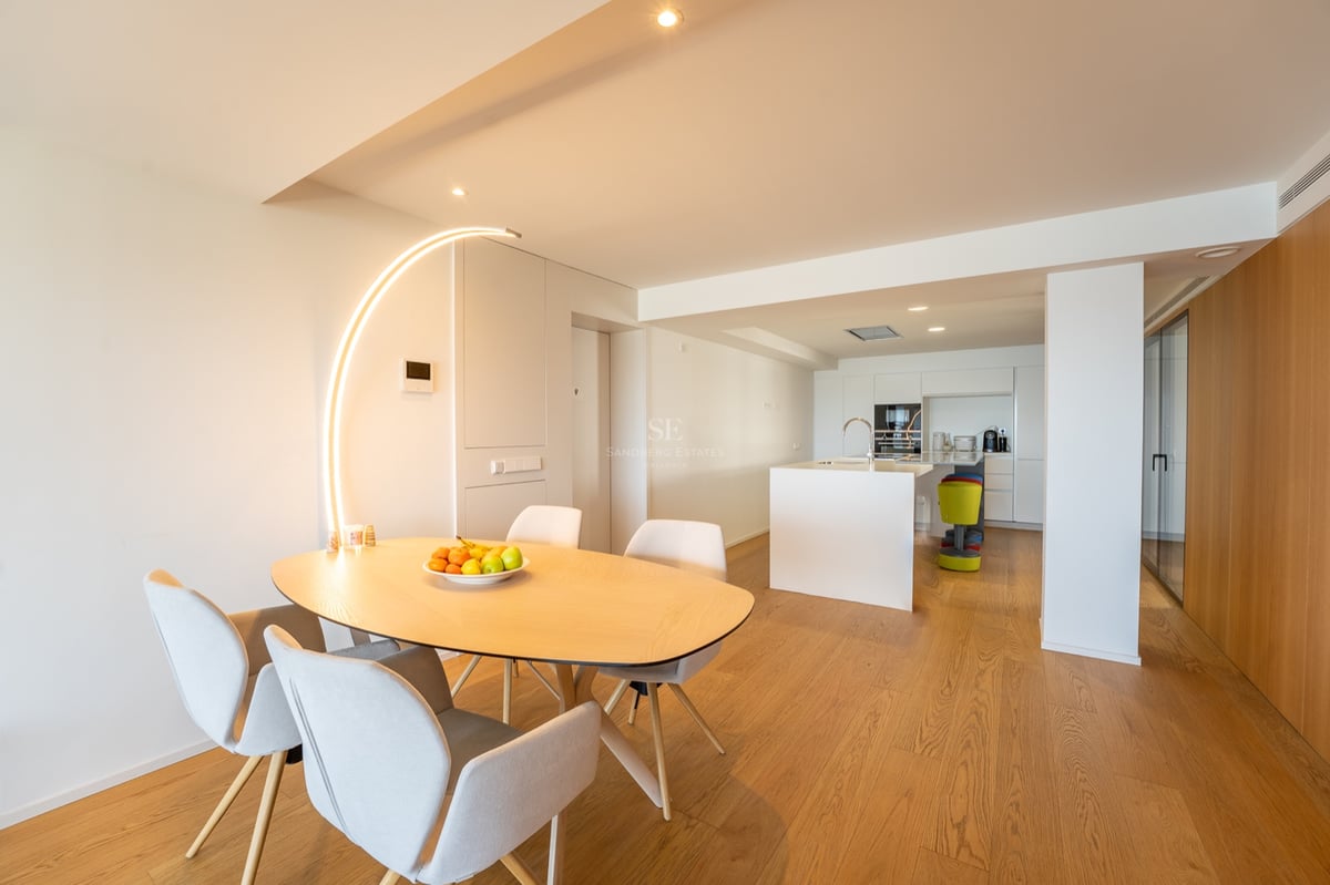 Minimalistisk matplats med bord i ljust trä, grå stolar och en iögonfallande båggolvlampa.