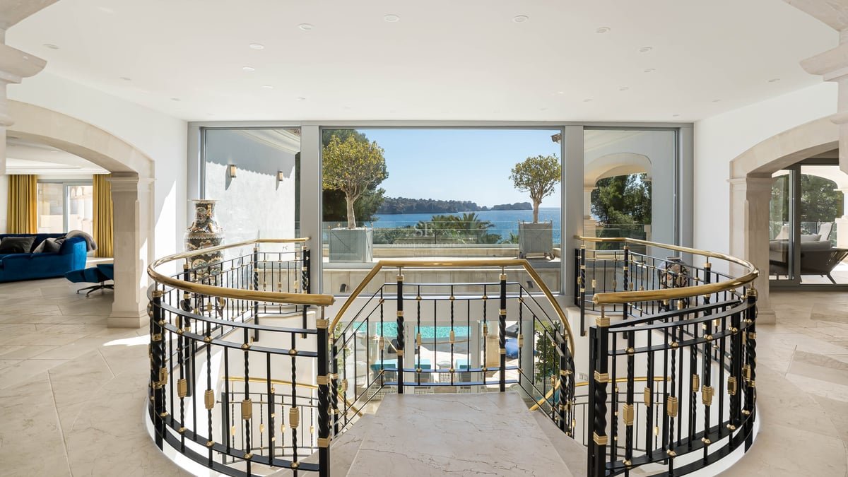 Innenansicht eines Marmortreppenhauses mit kunstvollem Geländer und Blick durch große Fenster auf das Meer.