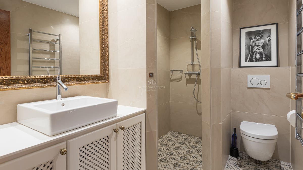 Modern bathroom featuring white vanity, ornate gold mirror, walk-in shower, and patterned floor tiles.