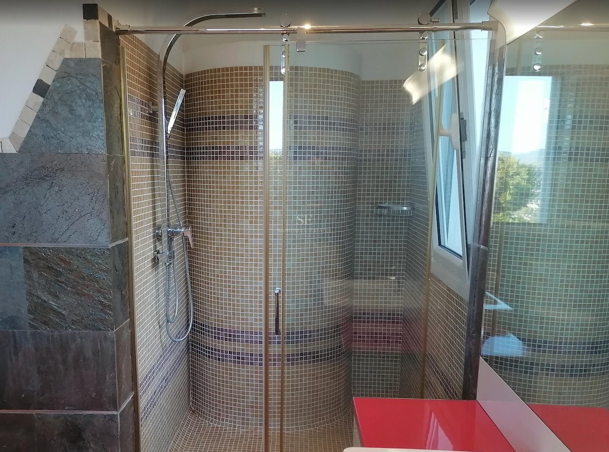 Une cabine de douche en verre avec des carreaux de mosaïque beiges, une robinetterie chromée et un mur courbe.