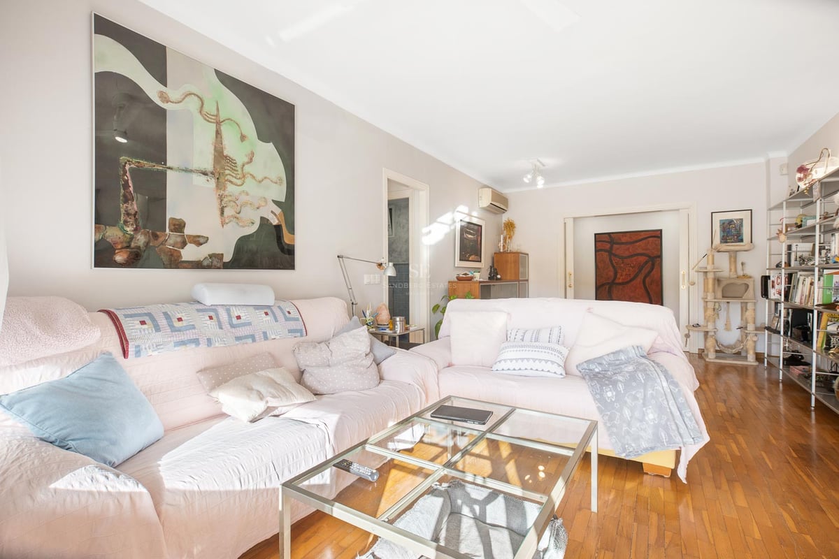 Helles Wohnzimmer mit rosa Sofas, Glastisch, poliertem Parkett und großen Wandgemälden.