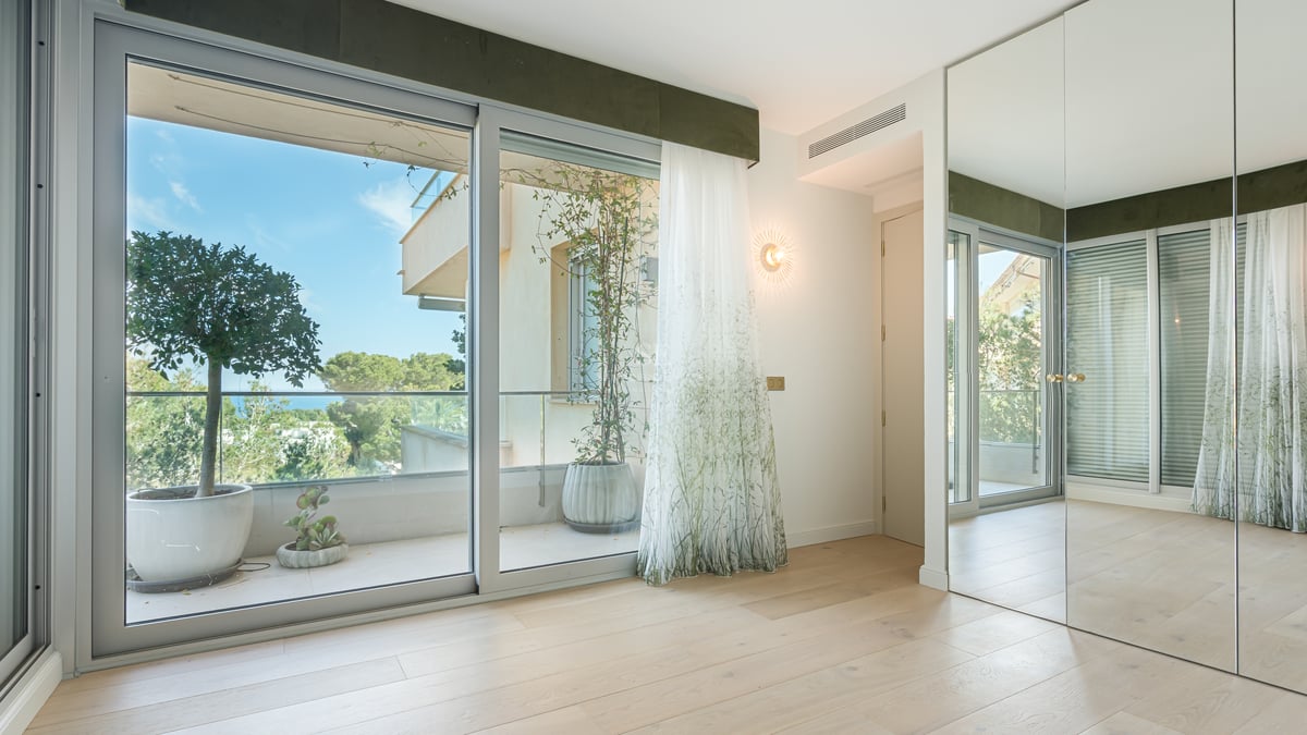 Bright bedroom with oak floors, mirrored wardrobes, and sliding glass doors opening to a terrace with garden views.