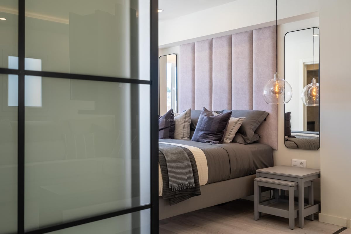 Detailansicht eines Hauptschlafzimmers mit rosa gepolstertem Kopfteil, Glaspendelleuchten und schwarzer Glastrennwand.