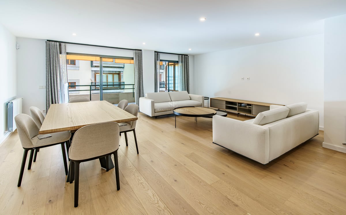Séjour ouvert avec canapés blancs, table à manger en bois et grandes baies vitrées donnant sur un balcon.