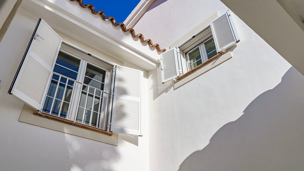 Detaljbild av vit fasad med mallorkinska fönsterluckor, terrakottatakpannor och fönsterbrädor i natursten.