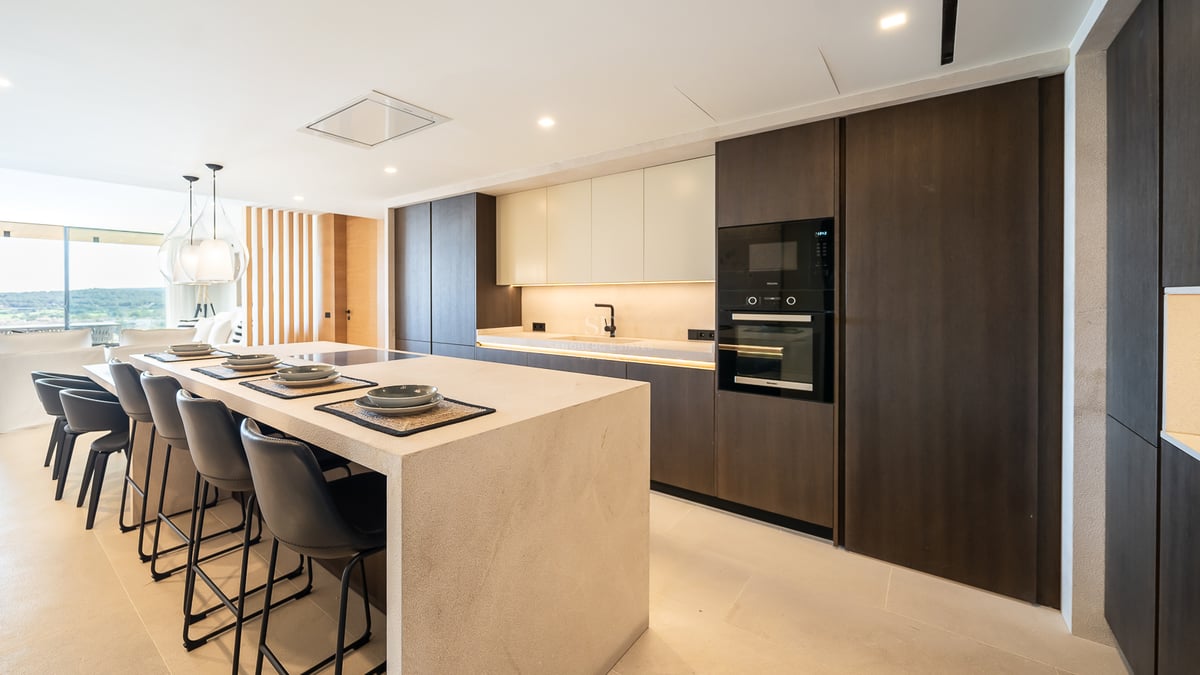 Cuisine moderne à aire ouverte avec un grand îlot en pierre, des armoires en bois sombre et des fours encastrés.