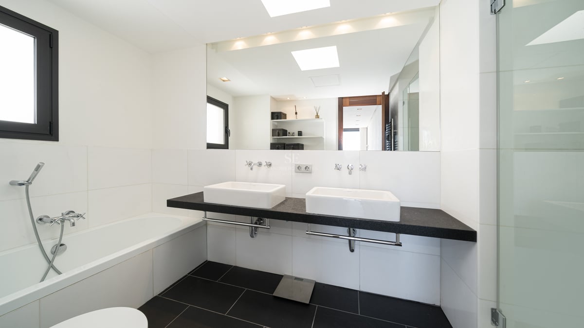 Bright modern bathroom featuring a black floating double vanity, white ceramic sinks, large mirror, and glass shower.