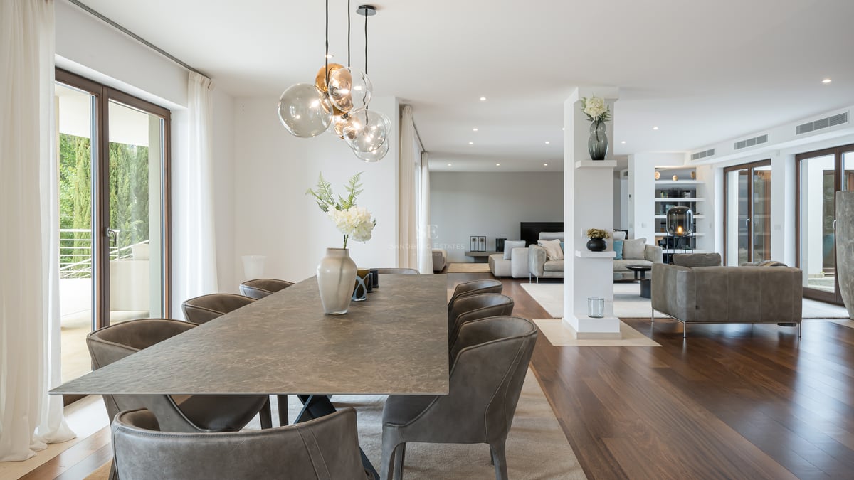 Grande table à manger en pierre avec chaises en cuir dans une pièce lumineuse avec parquet et baies vitrées.