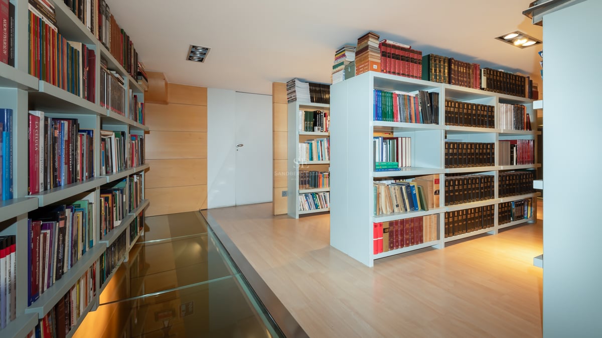 Bibliothèque moderne avec étagères blanches et passerelle en verre transparent sur parquet en bois clair.