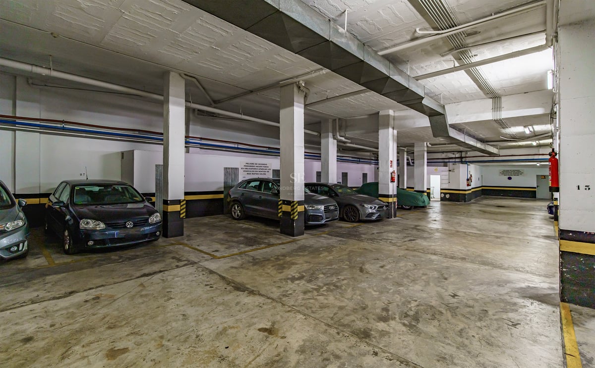 Grand garage souterrain avec piliers en béton, marquages de sécurité jaunes et voitures garées.