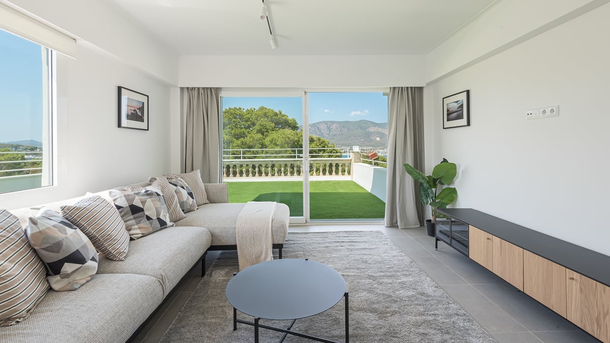 Salon moderne avec canapé d'angle gris et baies vitrées ouvrant sur une terrasse et un paysage de montagnes.