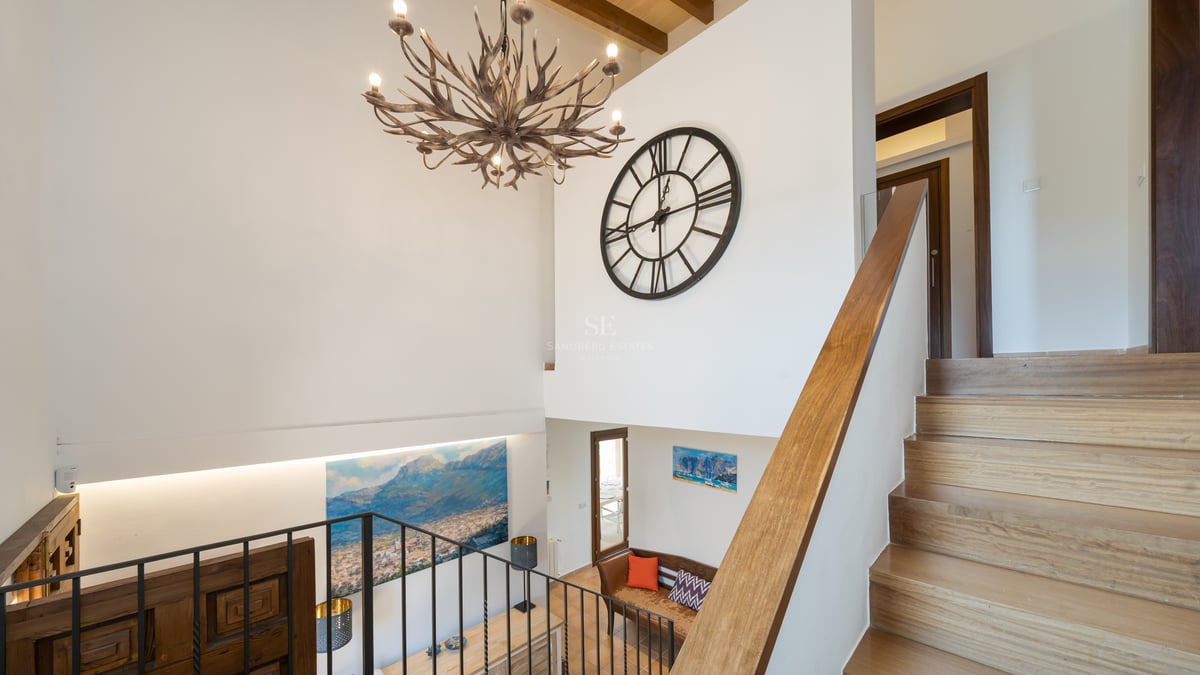 Vue intérieure d'un escalier en bois avec un grand lustre en bois de cerf et une horloge murale décorative.