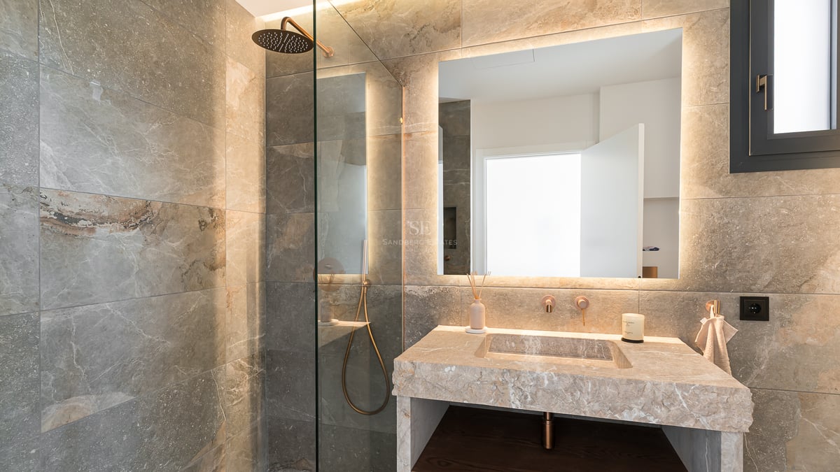 Luxuriöses Badezimmer mit begehbarer Glasdusche, Steinwaschtisch und großem hinterleuchtetem Spiegel mit warmem Licht.