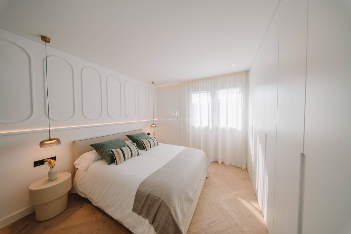 Chambre principale moderne avec lit double, moulures murales décoratives et parquet clair en point de Hongrie.