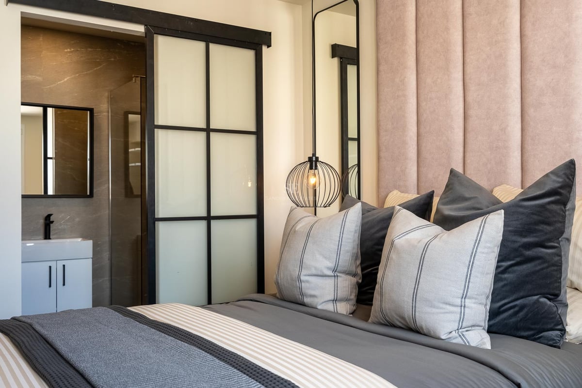 Schlafzimmer mit rosa Samtkopfteil, Designerlampe und industrieller Schiebetür zum Badezimmer.