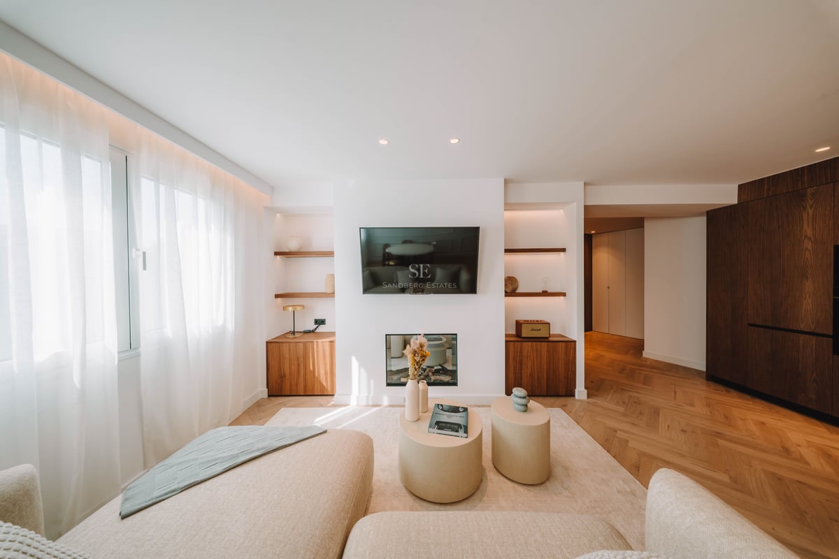 Salon lumineux avec TV murale, cheminée, parquet en point de Hongrie et canapés beiges.