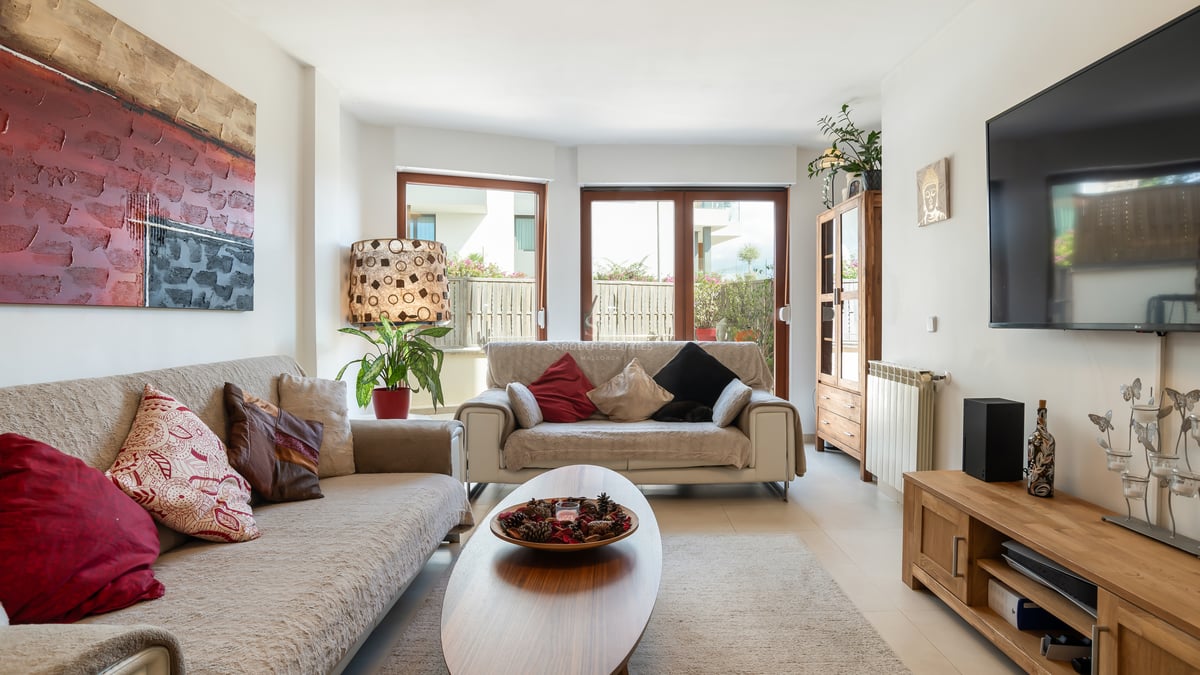 Un salon ensoleillé avec des canapés beiges, des meubles en bois et des baies vitrées ouvrant sur une terrasse.
