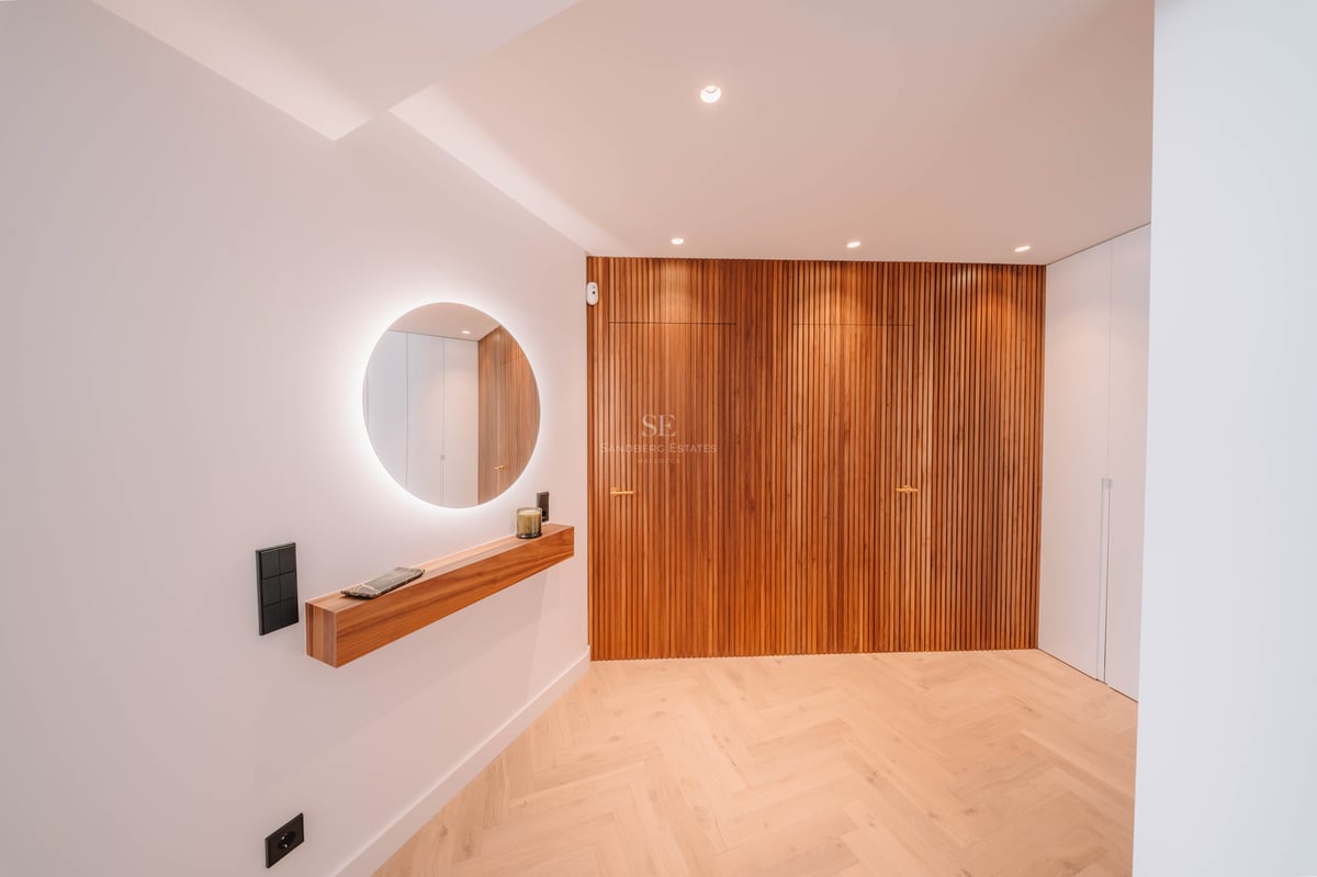Couloir minimaliste avec miroir rétroéclairé, étagère en bois et mur en lattes verticales.