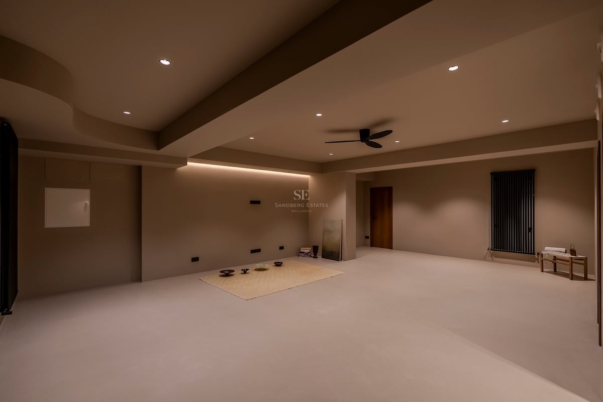 Une grande pièce minimaliste aux murs et sols beiges, avec éclairage encastré et ventilateur de plafond.