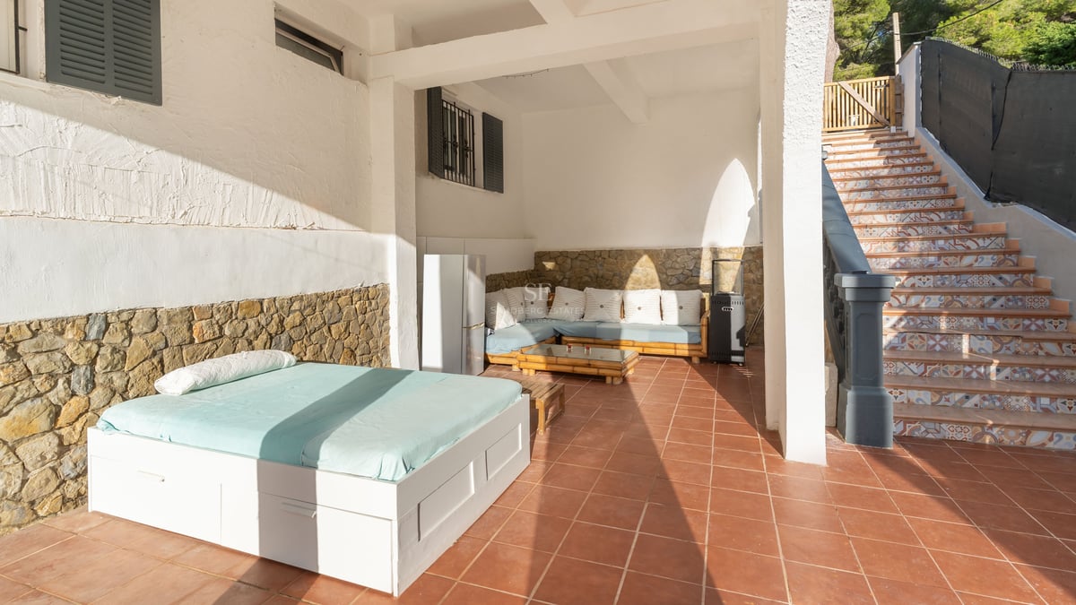 Terrasse couverte avec sols en terre cuite, lit de jour extérieur, banquette, murs en pierre et escalier carrelé.