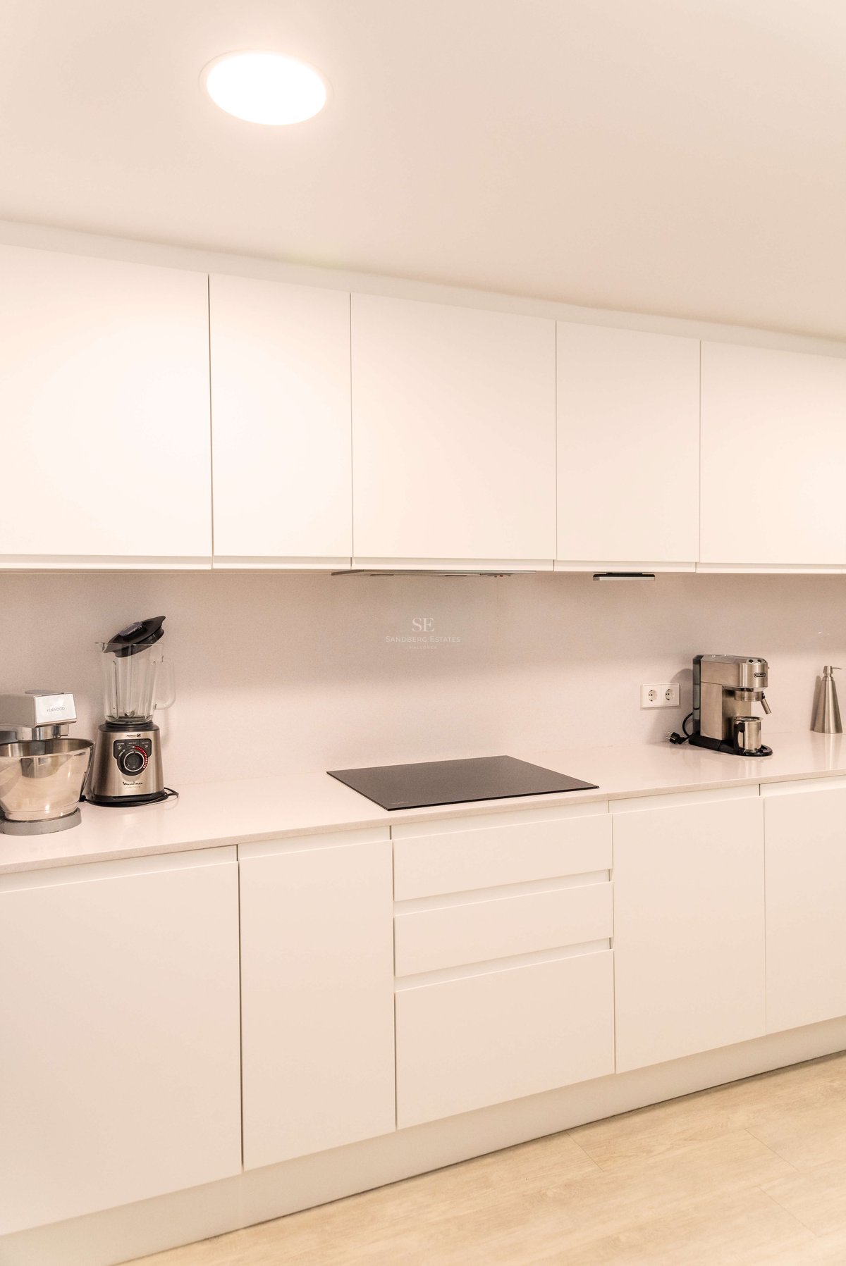 Zeitgenössische weiße Küche mit grifflosen Schränken, Quarzarbeitsplatte und Induktionskochfeld.