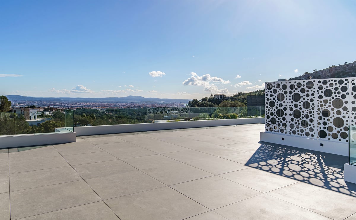 Grand toit-terrasse moderne avec dalles grises, garde-corps en verre et écran blanc perforé dominant la ville.