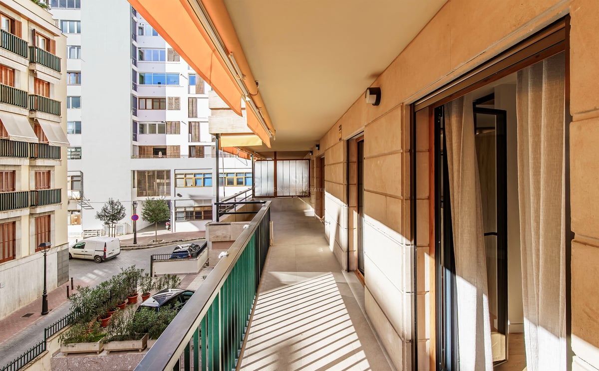 Long balcon ensoleillé avec auvent orange et balustrade métallique donnant sur une rue urbaine.