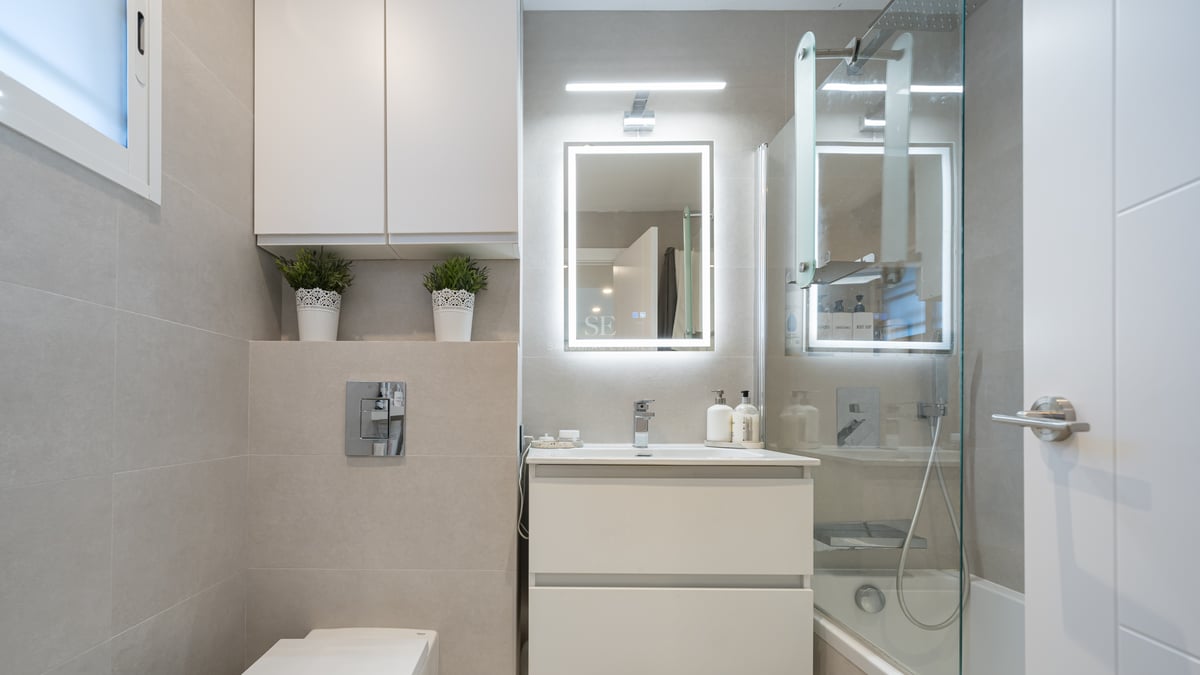 Modern bathroom with white vanity, backlit LED mirror, glass shower screen, and beige large-format tiles.