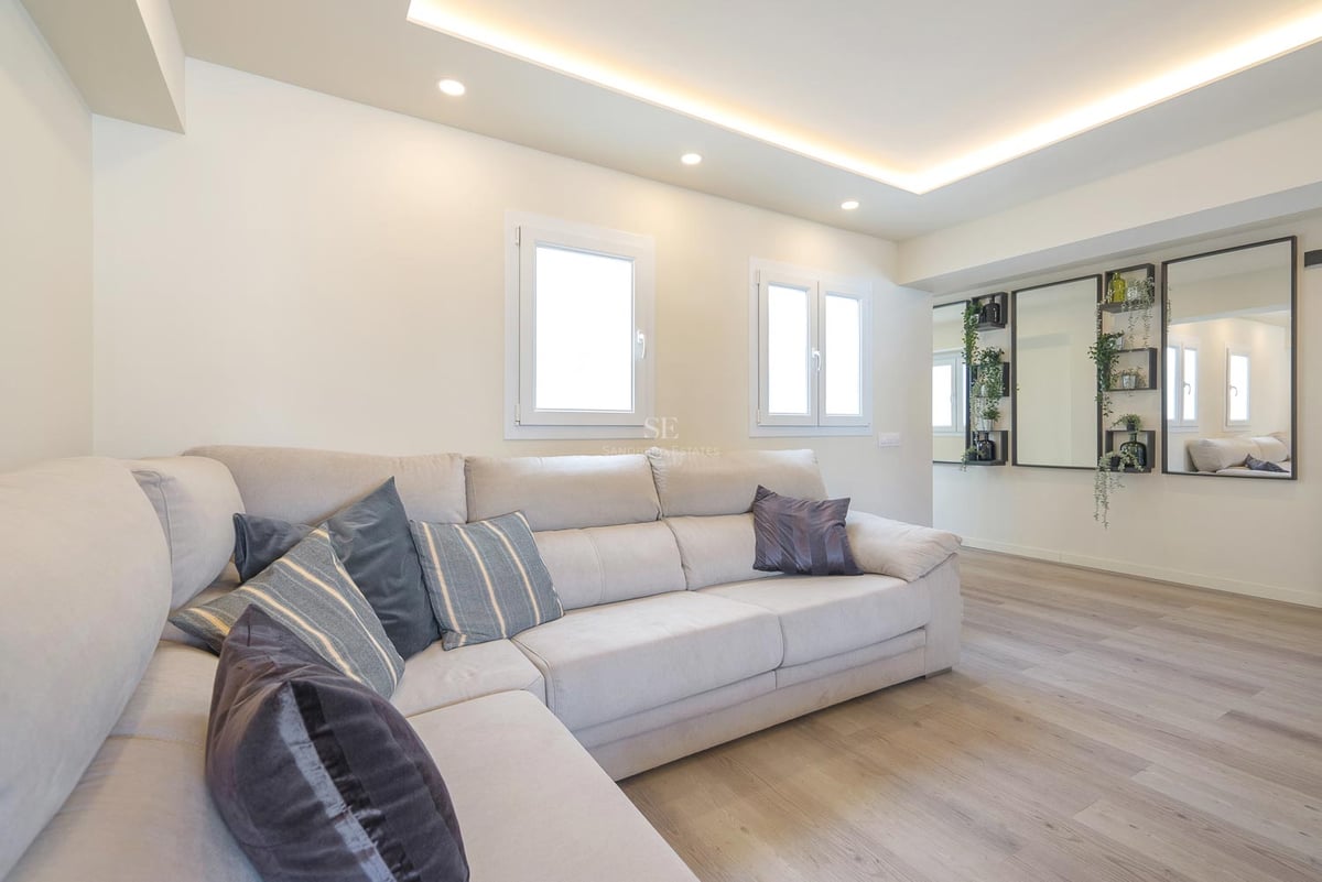 Modernes Wohnzimmer mit großem cremefarbenem L-Sofa, hellem Holzboden und LED-Deckenbeleuchtung.