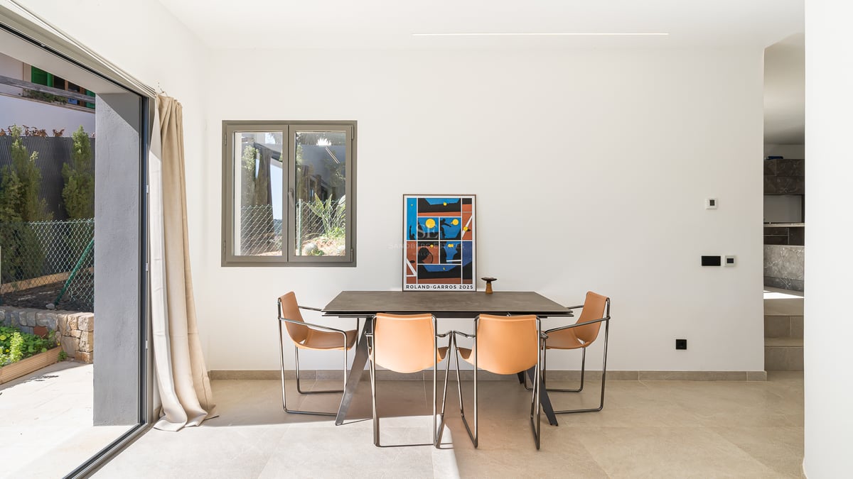 Modernt matrum med stenbord, läderstolar i cognac och stora skjutdörrar i glas mot en terrass.
