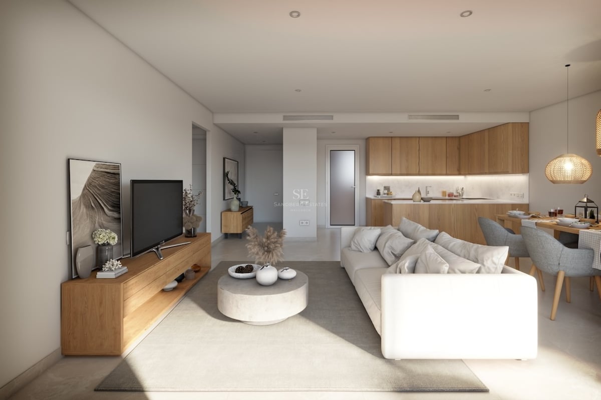 Bright modern living room with a white sofa, wooden furniture, and an integrated kitchen in the background.