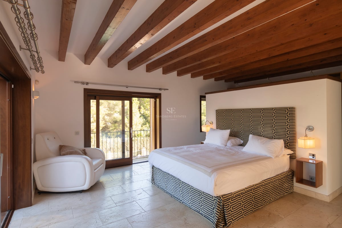 Huvudsovrum med rustika takbjälkar i trä, naturstensgolv och utgång till balkong.