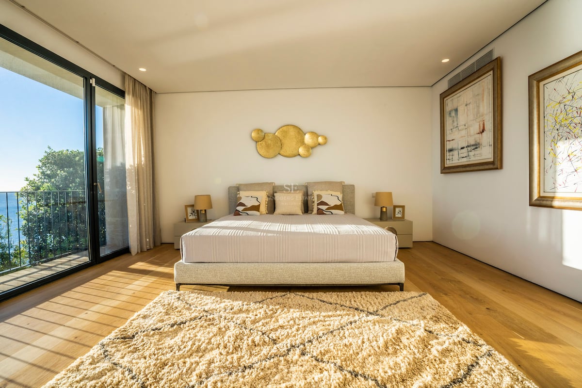 Modernes Hauptschlafzimmer mit Eichenparkett, bodentiefen Glasfronten und Zugang zur Terrasse mit Blick auf das Mittelmeer.