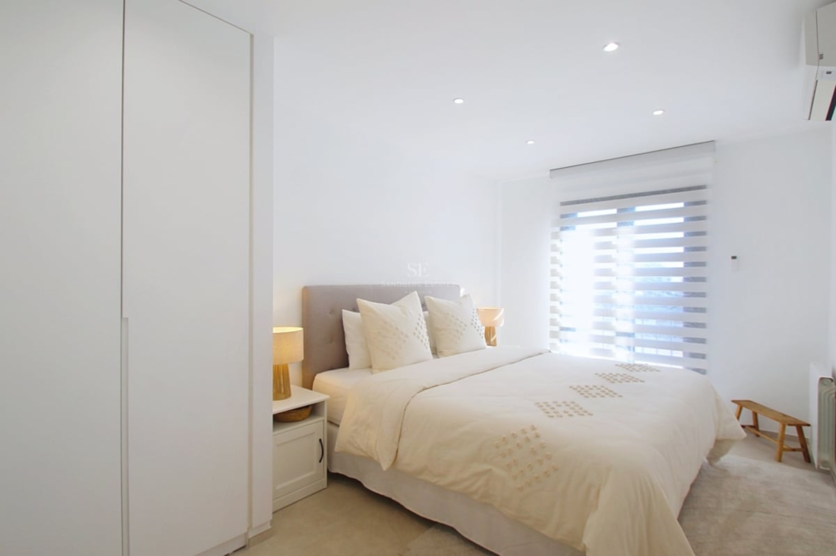 Välbelyst modernt sovrum i neutrala färger med dubbelsäng och vita inbyggda garderober.