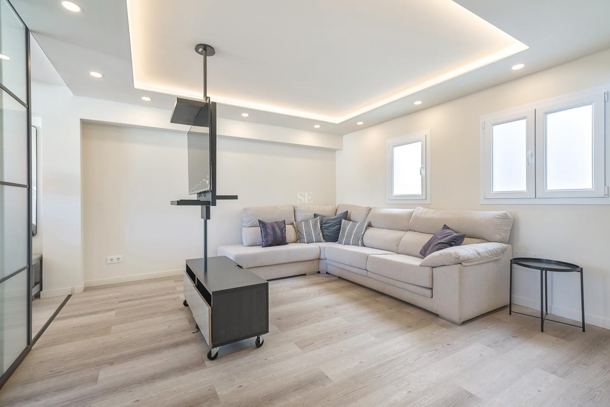 Modernes Wohnzimmer mit beige Ecksofa, hellem Holzboden und minimalistischer schwarzer TV-Halterung.