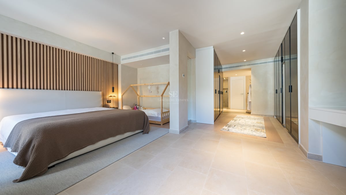 Chambre principale moderne avec tête de lit en lattes de bois, sol en pierre et placards en verre noir.