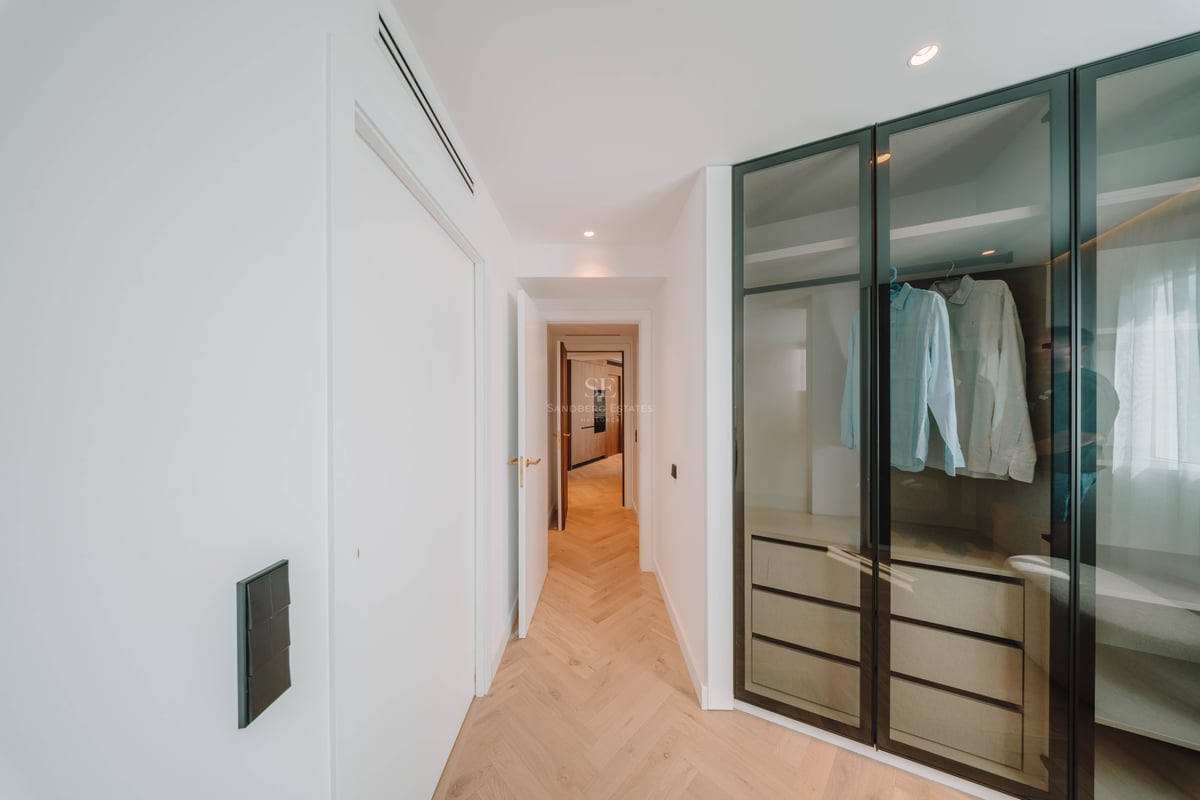 Couloir moderne avec parquet en chevrons menant à un dressing doté de portes vitrées aux cadres noirs.