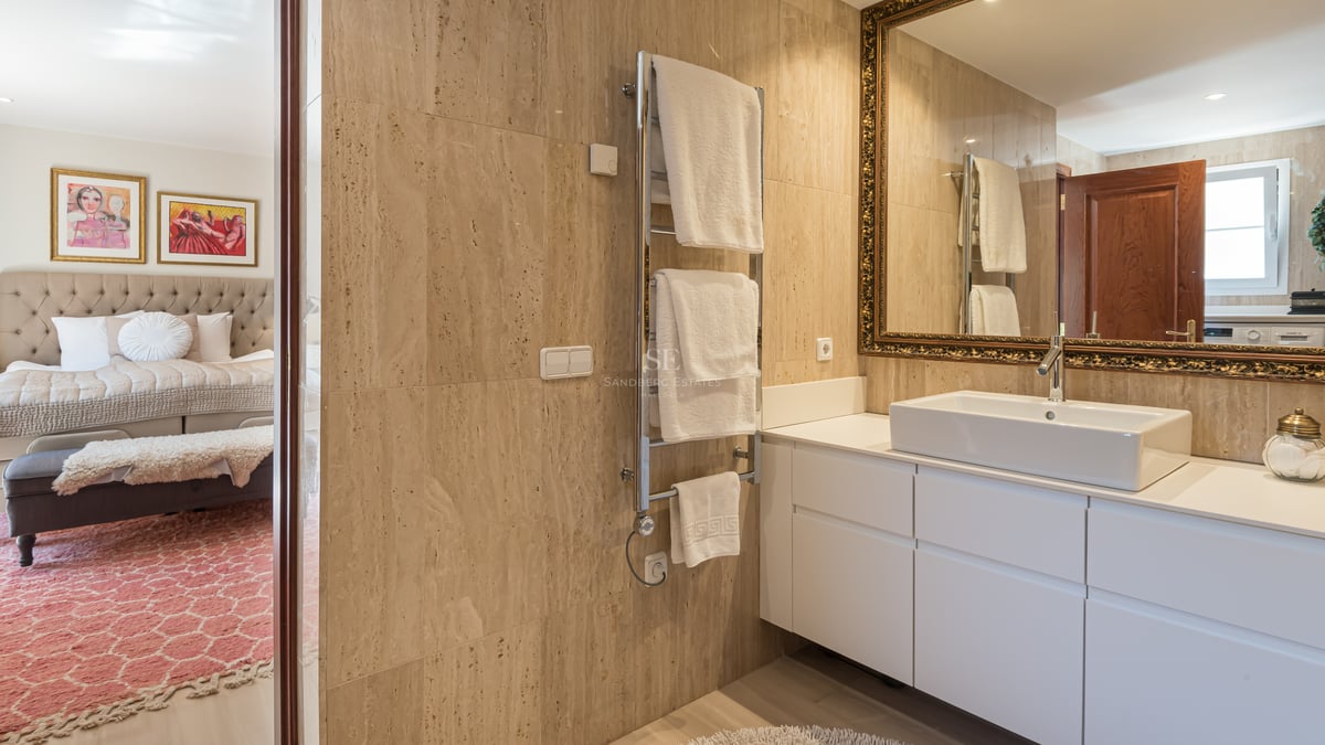 Modern bathroom with travertine stone walls, white vanity, vessel sink, and an ornate gold-framed mirror.