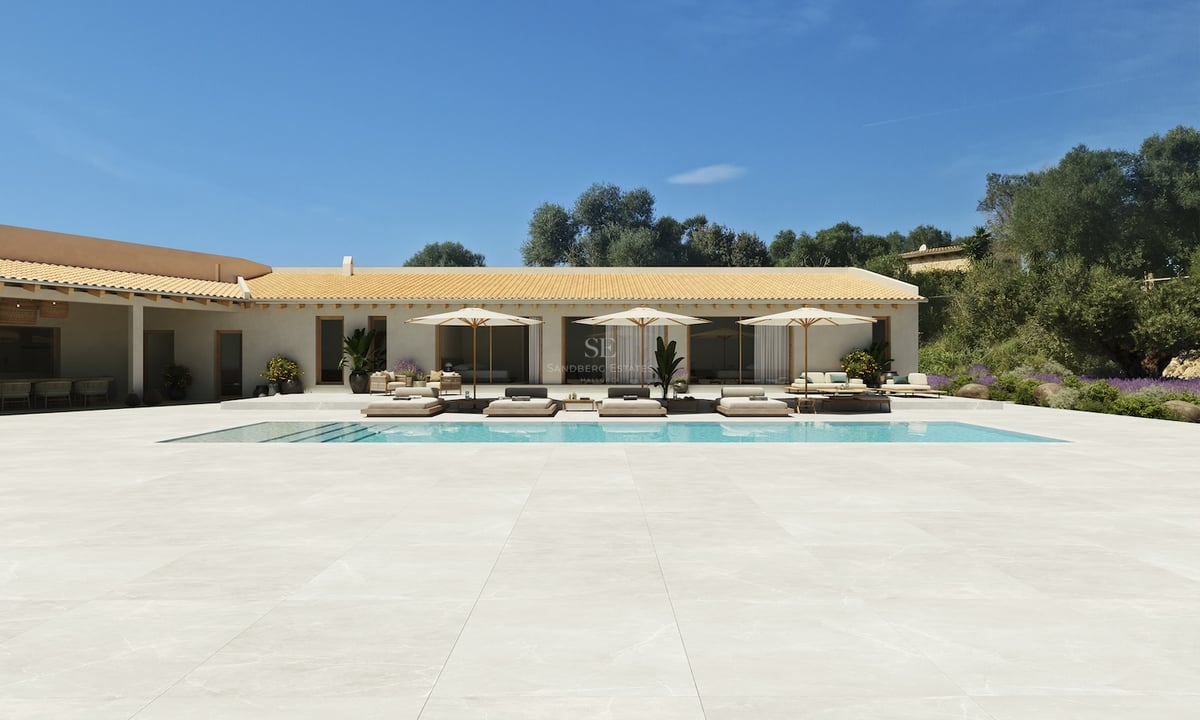 Grande piscine et vaste terrasse claire devant une villa méditerranéenne sous un ciel bleu pur.