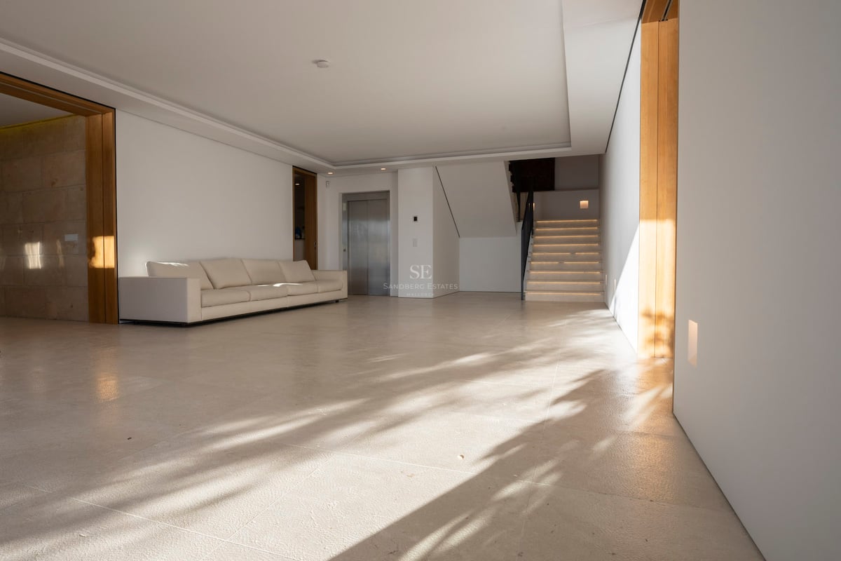 Großzügige minimalistische Halle mit cremefarbenen Steinböden, weißem Sofa, privatem Aufzug und Steintreppe.