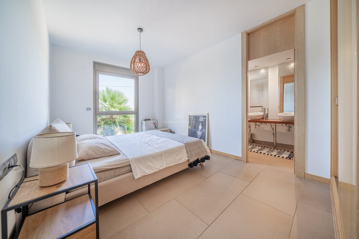 Chambre lumineuse avec accents de bois clair, salle de bains attenante et vue sur les palmiers.