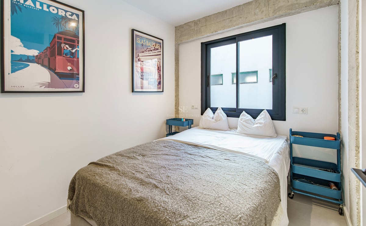 Chambre moderne avec lit double, poutres en béton, dessertes bleues et affiches de voyage vintage.