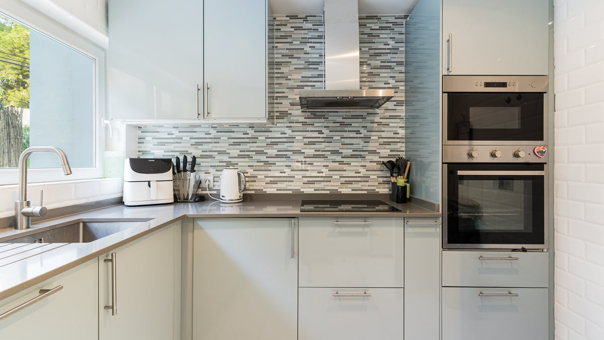 Cuisine moderne avec des armoires bleu clair, des plans de travail gris et une crédence en mosaïque.