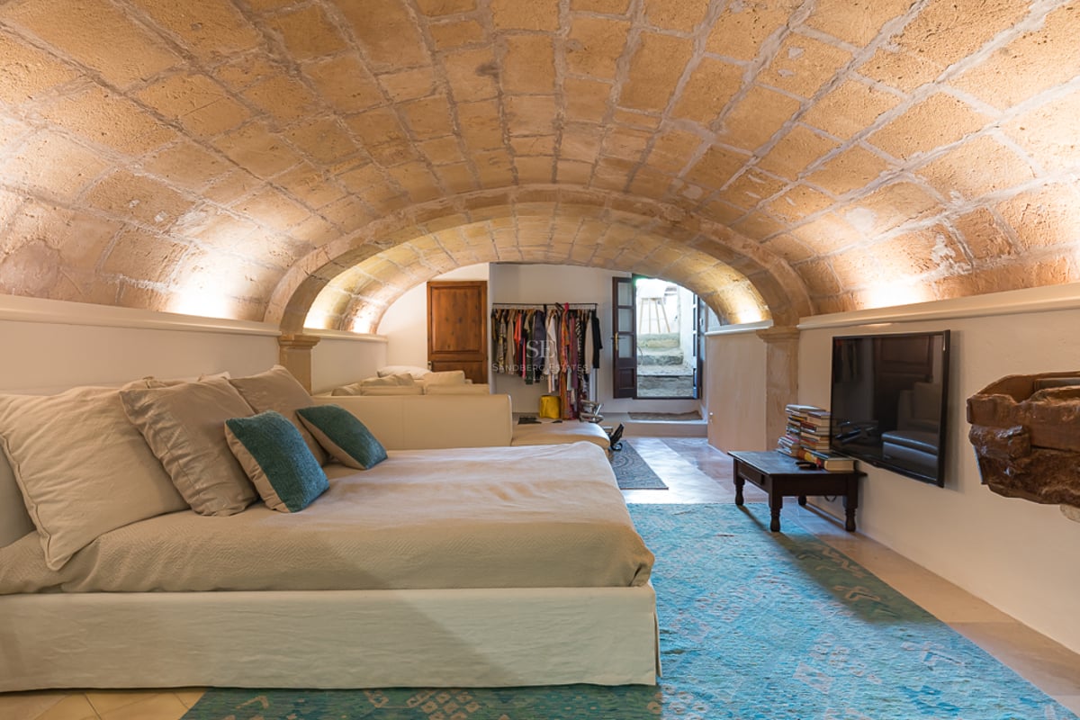 Chambre avec plafond voûté en pierre naturelle, grand lit avec touches de turquoise et éclairage indirect chaleureux.