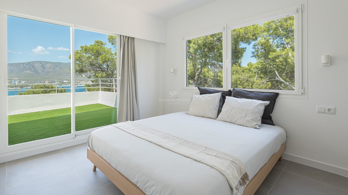 Chambre moderne avec lit double et baies vitrées ouvrant sur une terrasse avec vue sur mer et montagne.