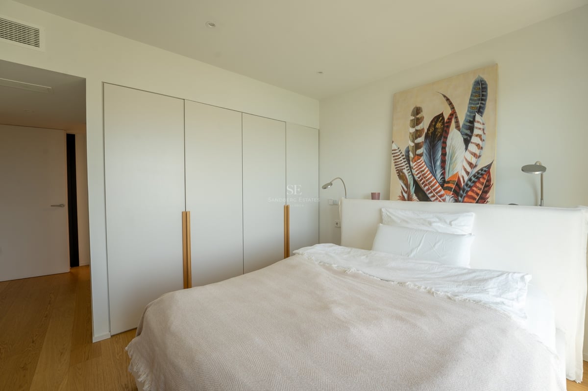 Ljust sovrum med vit säng, stora inbyggda garderober med trädetaljer och en tavla med fjädrar.