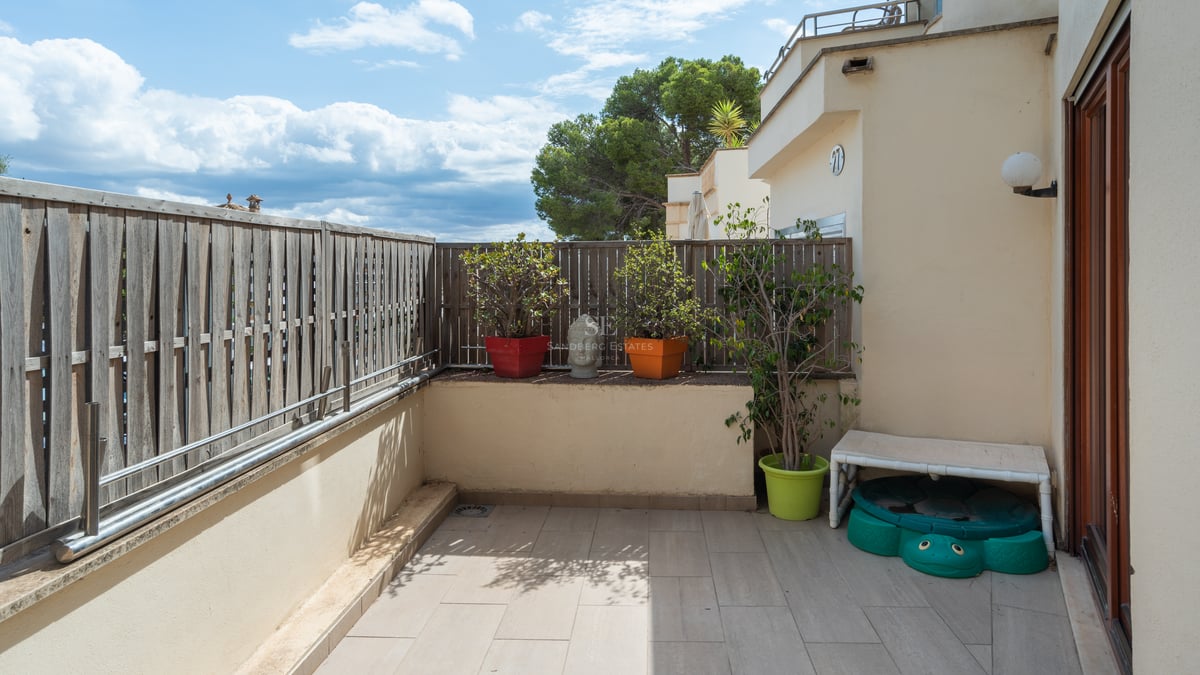 Terrasse privée carrelée avec clôture en bois, plantes en pots et vue sur la végétation sous un ciel bleu.