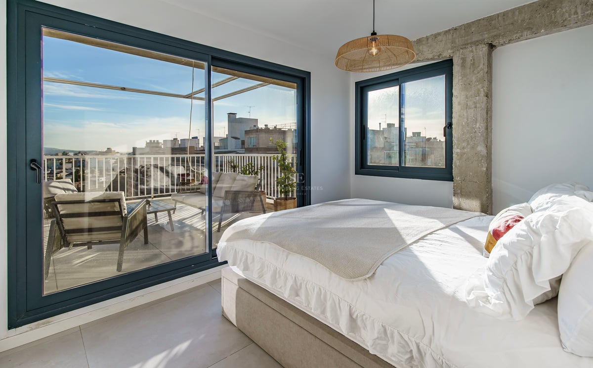 Chambre lumineuse avec lit blanc et grandes baies vitrées coulissantes ouvrant sur une terrasse privée avec vue.